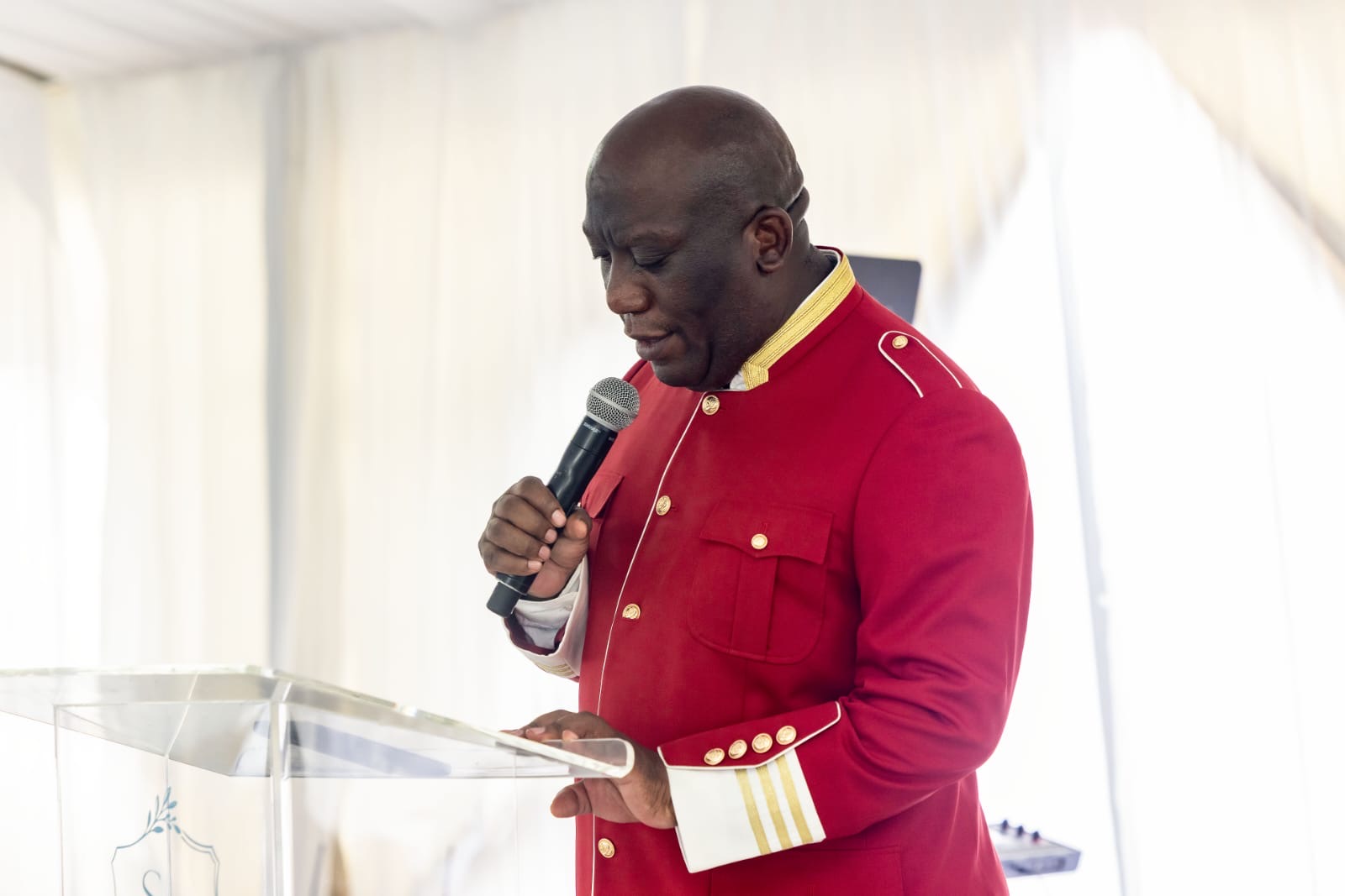 Bishop Mogodiri in prayer at the pulpit in his red ceremonial jacket